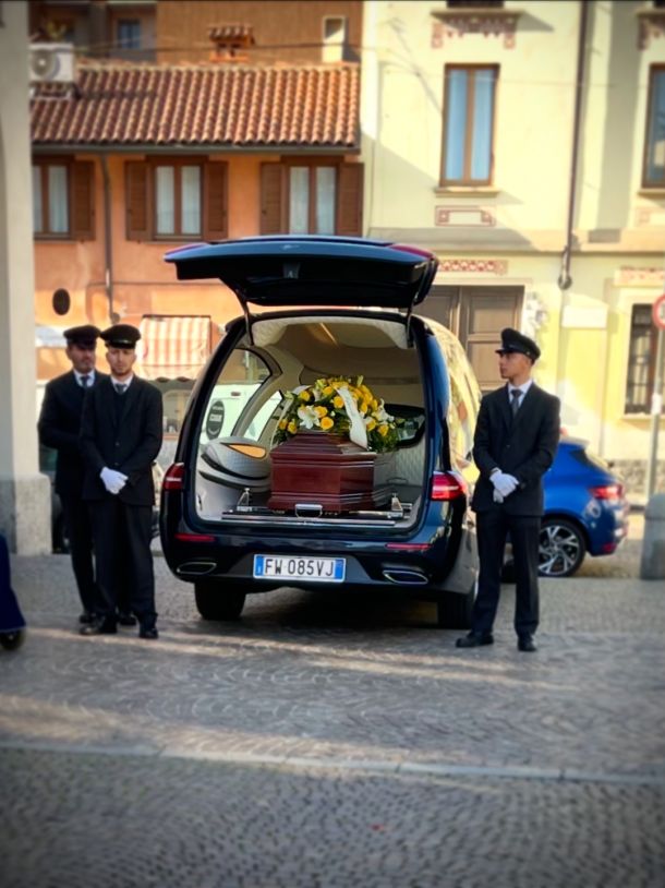 Carro funebre Mercedes-Benz nero con addobbo floreale per servizio funebre con Onoranze Funebri Musocco in un cimitero a Milano